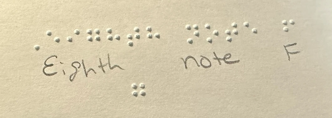 Close-up of embossed braille on paper with the handwritten annotation “Eighth note F.”